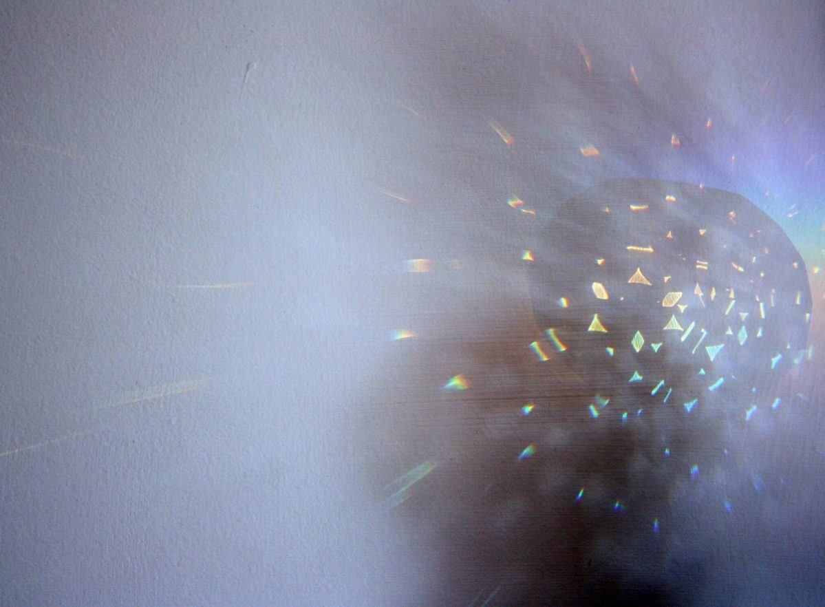 Refraction of Light is a photograph by artist Priti Patel. It shows an explosion from a dark ball. The rainbow coloured light show signs and symbols shooting out from the ball. The background is blue in colour.